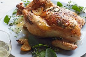 Lemon-thyme roast chicken, served on a white plate surrounded by fresh bay leaves and other green herbs.