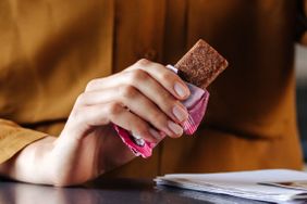 Hand holding a snack wrapped in paper near a table