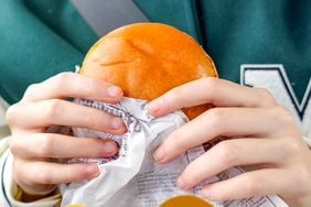 A child in a green and white varsity jacket holds a McDonald's hamburger.