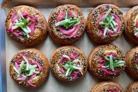 Baked pastries topped with pickled vegetables and herbs on a tray