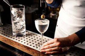 A person preparing a martini with an olive garnish