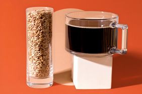 A glass of barley grains next to a clear mug of dark liquid set against a minimalist background
