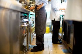 Chefs working in a commercial kitchen area with one in an apron and professional footwear