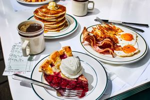 A table with pancakes a slice of cherry pie with ice cream eggs bacon hash browns and coffee diner breakfast foods