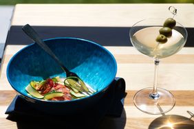 A bowl containing a salad served with an olive garnish martini on a wooden table