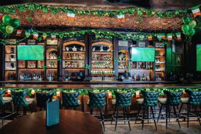 A pubs interior decorated for St Patricks Day featuring a bar counter shelves with bottles green chairs and Irishthemed decorations