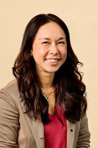 A person smiling wearing a blazer and shirt posed against a neutral background