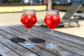Two glasses of campari spritz on a wooden table outdoors