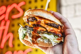A hand holding a cheeseburger with multiple layers of toppings and sauces