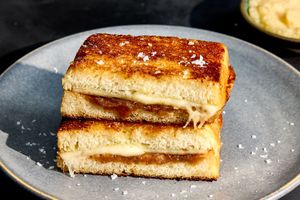 Stacked toast sandwiches filled with melted cheese and a layer of apple or fruit spread on a plate garnished with flakes of salt