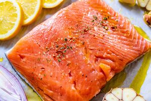 A raw salmon fillet seasoned with spices and garnished with vegetables and lemon slices ready for preparation