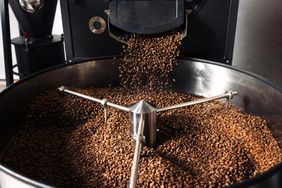 Coffee beans being poured into a large roasting machine with a metal agitator inside