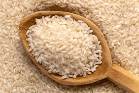 Spoonful of uncooked white rice with more rice in the background