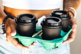 A person holding a tray with four lidded coffee cups