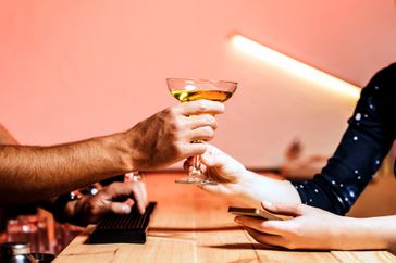 A bartender handing a cocktail to a patron across a bar counter