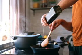 A person pouring oil into a pan while cooking on a stovetop