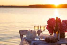 A sunset dining setup by a lake with wine glasses candles and flowers on a table