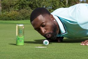 Dwyane Wade on a golf course blowing on a golf ball near a can of Cann THC drink