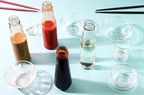 Assorted bottles of sauces and condiments with small serving dishes on a surface