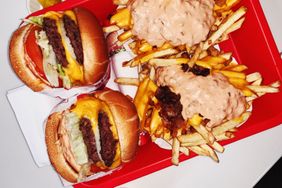 Two cheeseburgers and fries covered with sauce and toppings on a tray