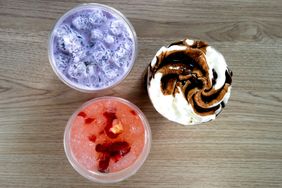 Three specialty drinks arranged on a wooden surface one creamy with chocolate topping one pink with fruit and one purple