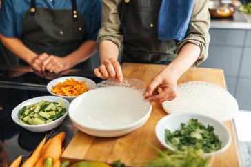 Two people making fresh spring rolls preparing ingredients and handling rice paper for wrapping