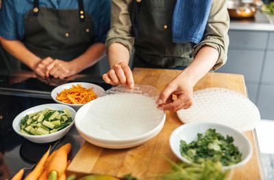 Two people making fresh spring rolls preparing ingredients and handling rice paper for wrapping