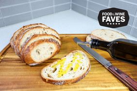 Oil flowing out of the Aozita Glass Olive Oil Dispenser onto a slice of bread on a cutting board