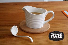 A ceramic gravy boat on a cork coaster with a matching ladle nearby on a wooden table