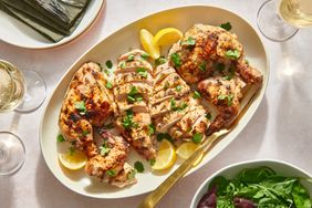 A platter of sliced yogurt marinated grilled chicken, served with lemon wedges and a green salad
