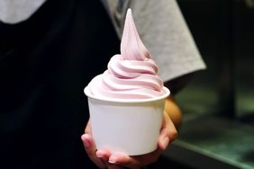 A person holding a cup of frozen yogurt with a swirl on top