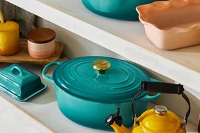Kitchenware including a teal Dutch oven a yellow kettle and other items on display on white shelves