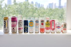 A lineup of various hard seltzer cans displayed on a ledge with a skyline visible in the background