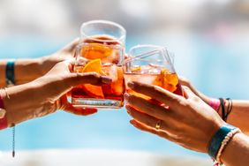 Four hands toasting with glasses of cocktails by a pool