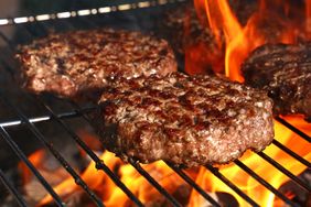 Hamburgers cooking on a grill with flames underneath