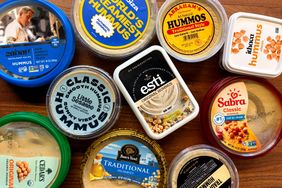 A collection of various hummus brands in packaging displayed on a wooden surface