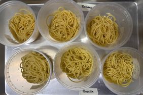 Six portions of cooked spaghetti in clear containers labeled with different brands