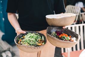 Person holding three bowls of food with various fresh ingredients