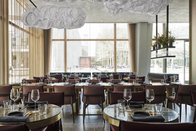 An elegantly arranged dining area with round tables and modern decor featuring hanging light fixtures resembling clouds