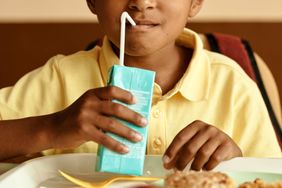 A child drinking from a juice box while sitting at a table with food