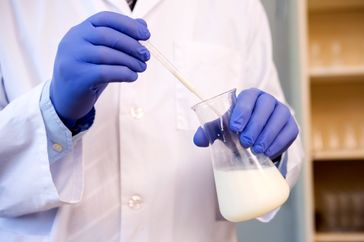 Scientist using a dropper with milk in a laboratory flask