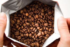 Open bag revealing roasted coffee beans held by two hands depicted from above
