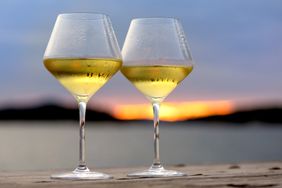 Two glasses of white wine on a table with a sunset in the background
