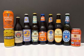 A lineup of nine Oktoberfestthemed beer bottles and cans shown on a white surface