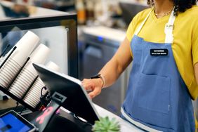 A barista wearing an apron operates a touchscreen at a coffee counter