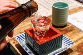 Sake being poured into a glass resting in a square wooden frame
