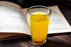 A glass of ginger tea on a table next to an open book