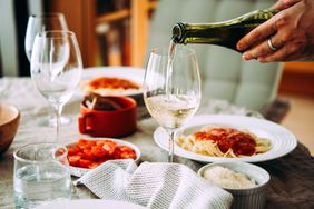 Wine being poured into a glass on a table set with food including pasta in tomato sauce and salad