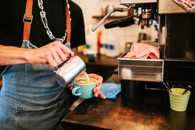 Barista preparing a latte at an espresso machine pouring steamed milk into a cup