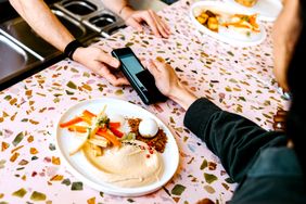 A person paying with a phone at a restaurant counter a plate of hummus and side dishes in view